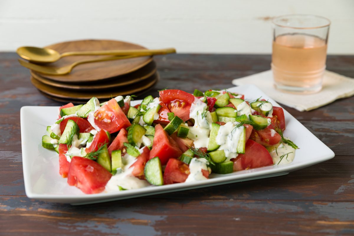 Sliced Creole tomatoes and sliced cucumbers arranged on a serving platter and topped with Feta Dressing