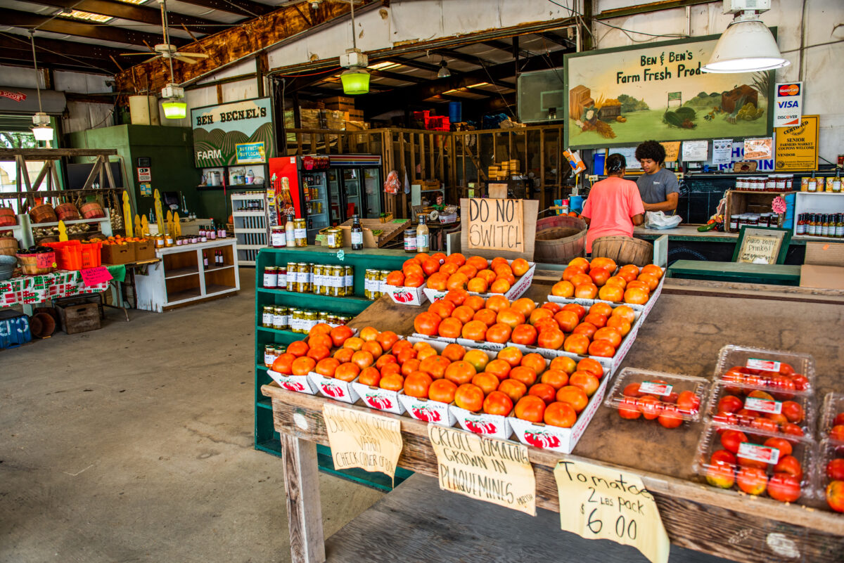 Ben and Ben Becnel's Market, shelves with jams, jellies and boxes of creole tomatoes with store sign in background.
