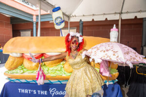 A member of the New Orleans Baby Dolls poses in front of Blue Plate's gigantic po-boy.